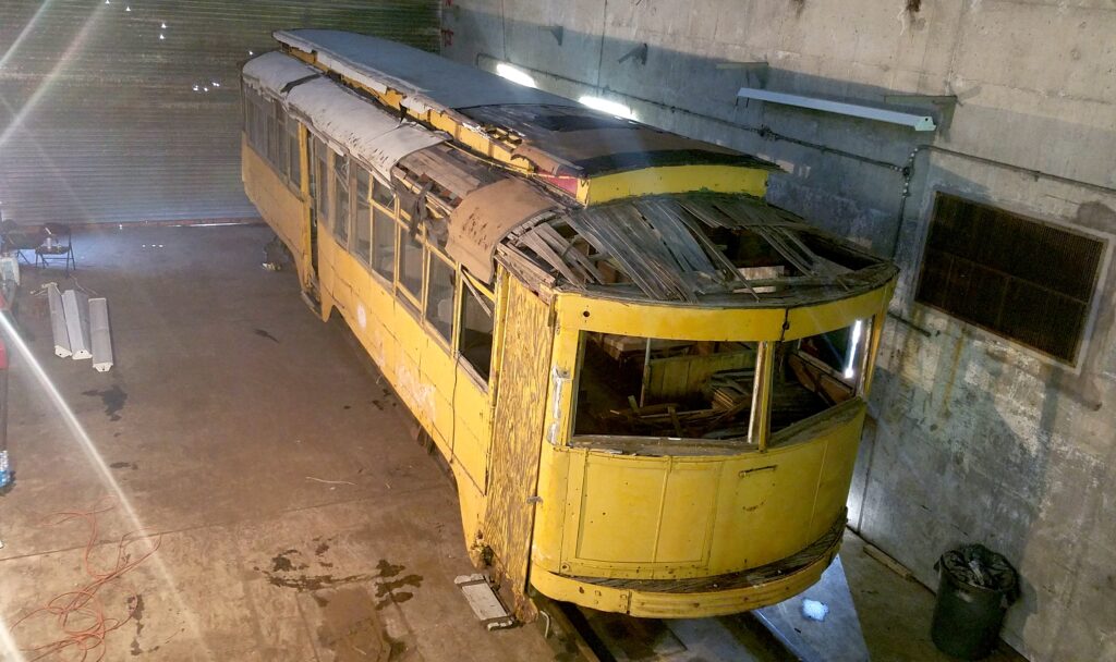 Trolley .04 in a warehouse awaiting restoration. The roof is partly missing and the front door boarded up with plywood.